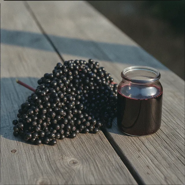 Grappe de baies de sureau noir et petit bocal de sirop violet foncé sur une planche en bois