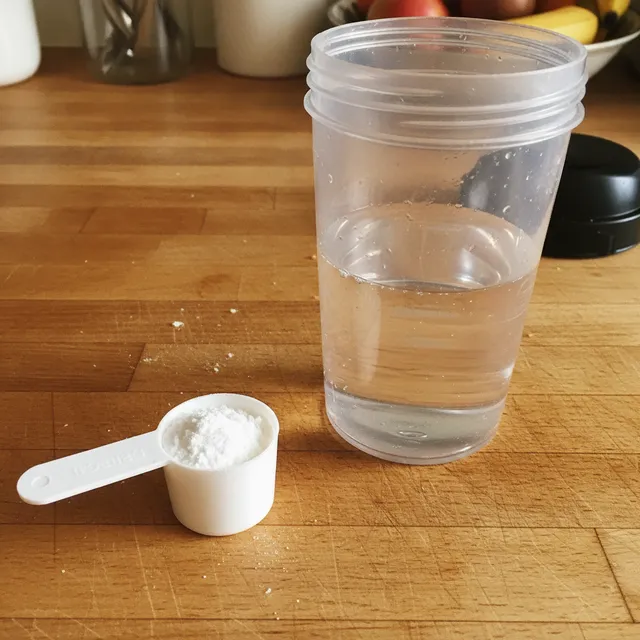 Une dosette de poudre de créatine à côté d'un shaker d'eau sur un plan de travail en bois