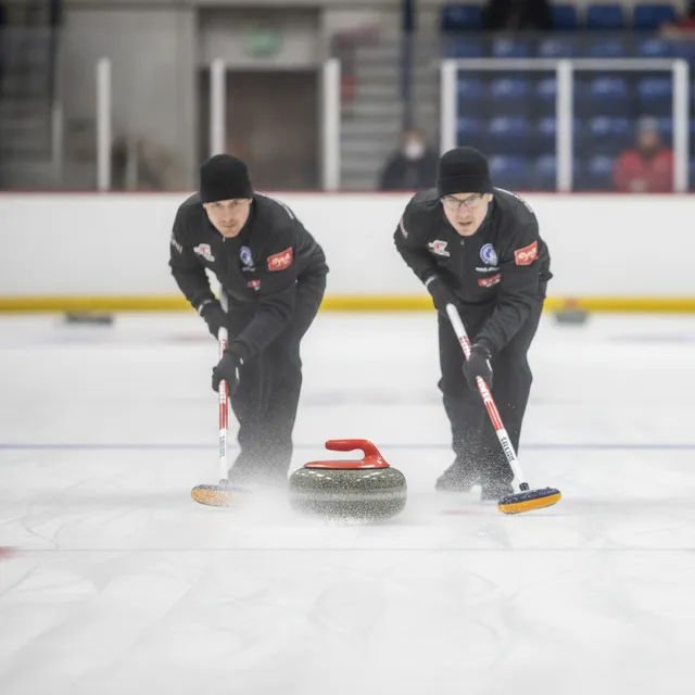 Deux balayeurs de curling frottent la glace devant une pierre de granite en pleine partie