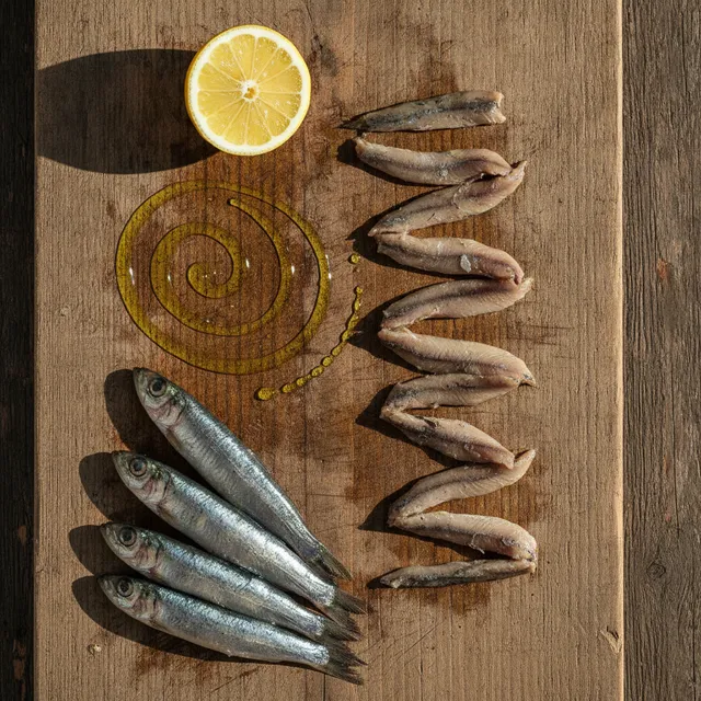 Anchois frais entiers et filets d'anchois marinés sur une planche en bois, avec un demi-citron et un filet d'huile d'olive