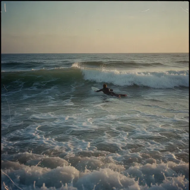 Un surfeur allongé rame sur sa planche à travers les vagues au coucher du soleil