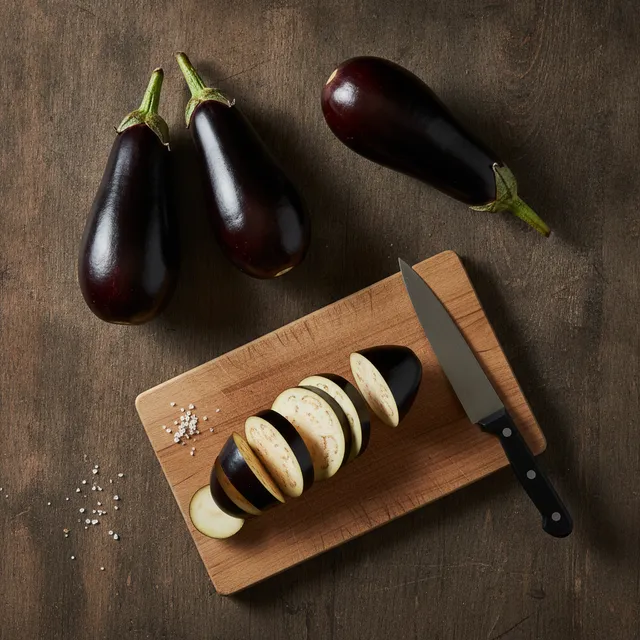 Trois aubergines violettes et des rondelles sur une planche en bois, vue de dessus