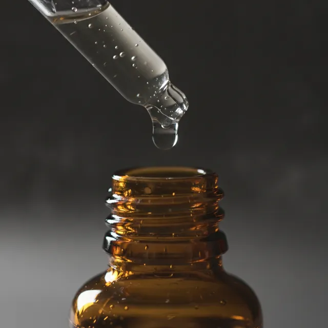 Pipette laissant tomber une goutte de serum au-dessus d'un flacon ambre, gros plan sur fond sombre