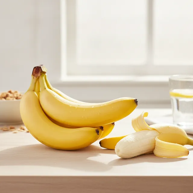 Régime de bananes mûres et une banane épluchée sur une table en bois clair