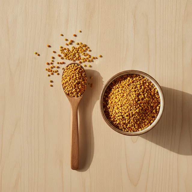 Pelotes de pollen d'abeille jaune orangé dans un bol en céramique et sur une cuillère en bois