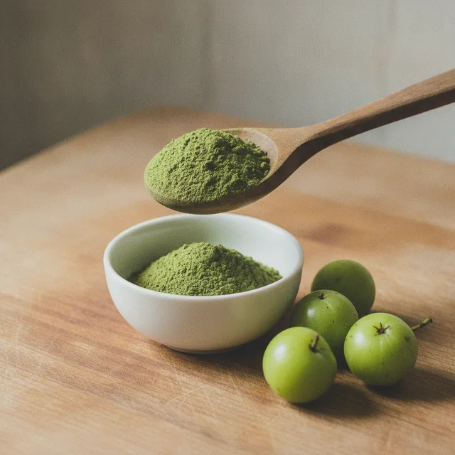 Poudre d'amla verte dans une cuillère en bois au-dessus d'un bol, avec des groseilles indiennes entières posées à côté