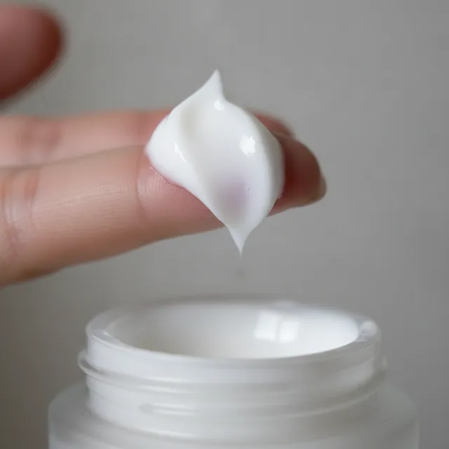 Noisette de creme blanche sur le bout d'un doigt au-dessus d'un pot de soin ouvert, gros plan macro