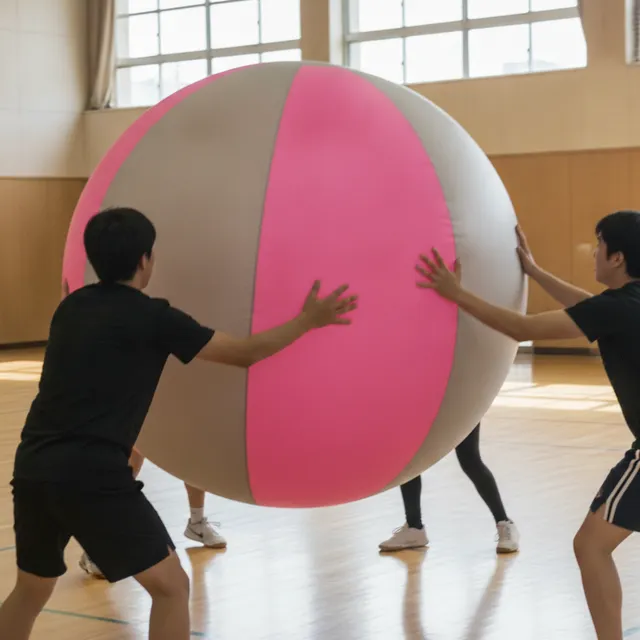 Énorme ballon de kin-ball gris et rose frappé par des joueurs dans un gymnase