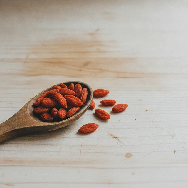 Baies de goji séchées rouge-orangé dans une cuillère en bois posée sur un plan de travail