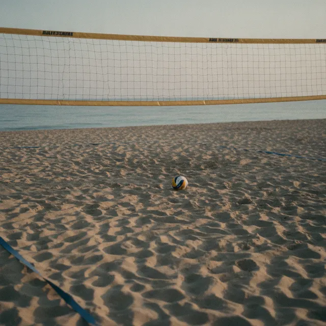 Terrain de beach-volley sur une plage en fin de journee, filet tendu et ballon pose dans le sable