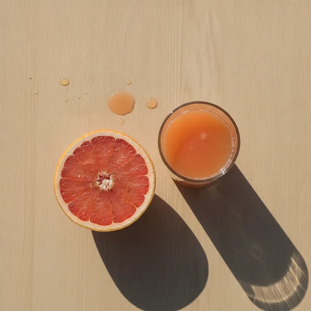 Un demi-pamplemousse rose et un verre de jus de pamplemousse posés sur une table en bois, vus de dessus