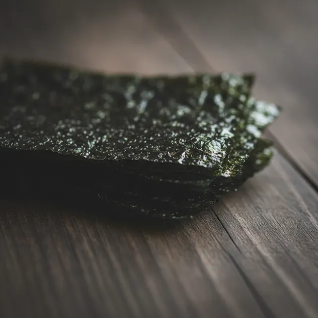 Pile de feuilles de nori séchées presque noires aux reflets vert foncé sur une planche en bois sombre