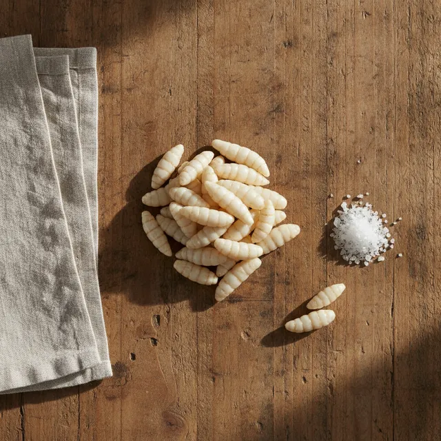 Petit tas de crosnes, tubercules blancs nacres en spirale, sur une table en bois avec un torchon en lin et du gros sel